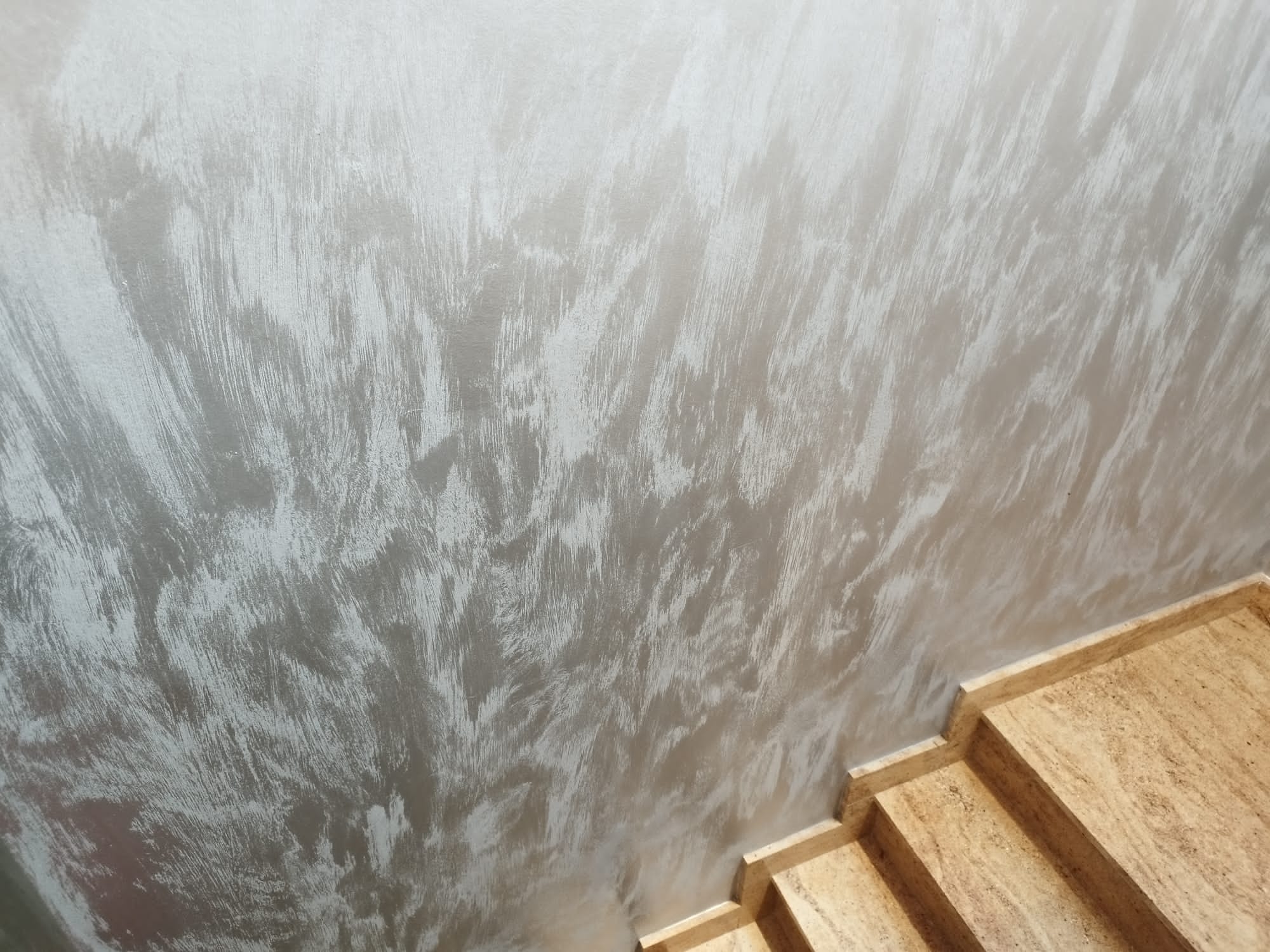 Dekoracyjna ściana wewnętrzna z efektem szczotkowanego srebra, widoczne fragmenty marmurowych schodów.