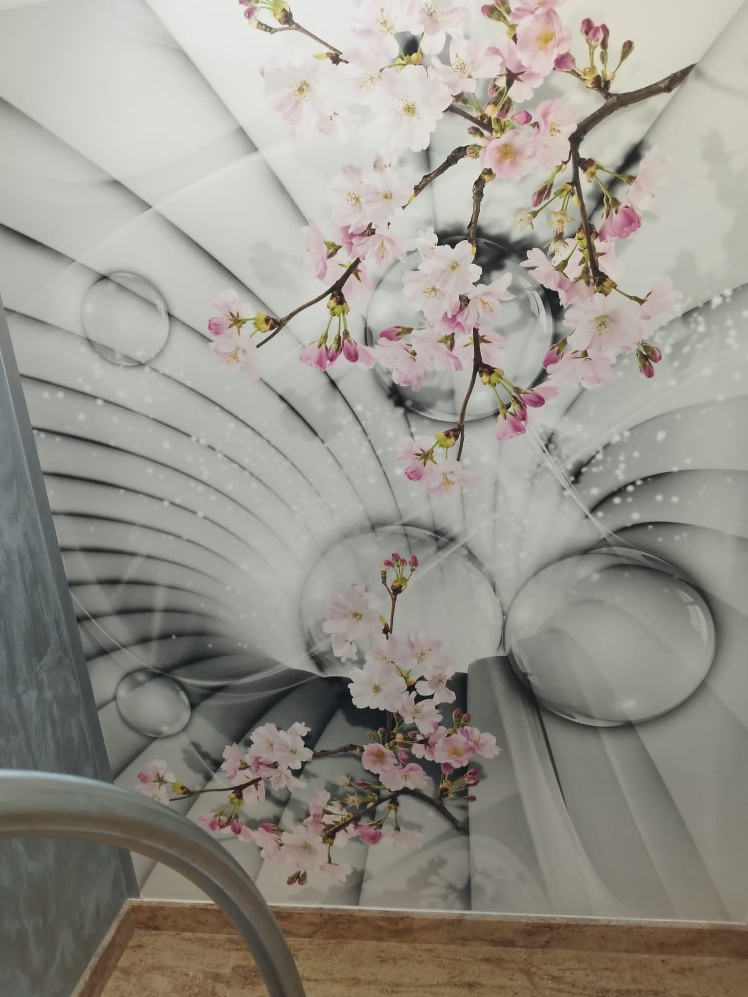 Dekoracyjny panel ścienny z motywem kwitnącej wiśni na abstrakcyjnym tle z okręgami, widoczne fragmenty poręczy i podłogi.
