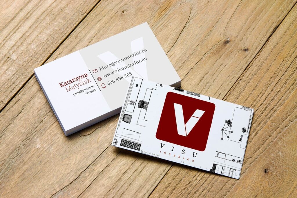 Dwie wizytówki na drewnianym tle: jedna z danymi kontaktowymi projektanta wnętrz Katarzyny Matysiak, druga z logo firmy VISU Interior i planem wnętrza.