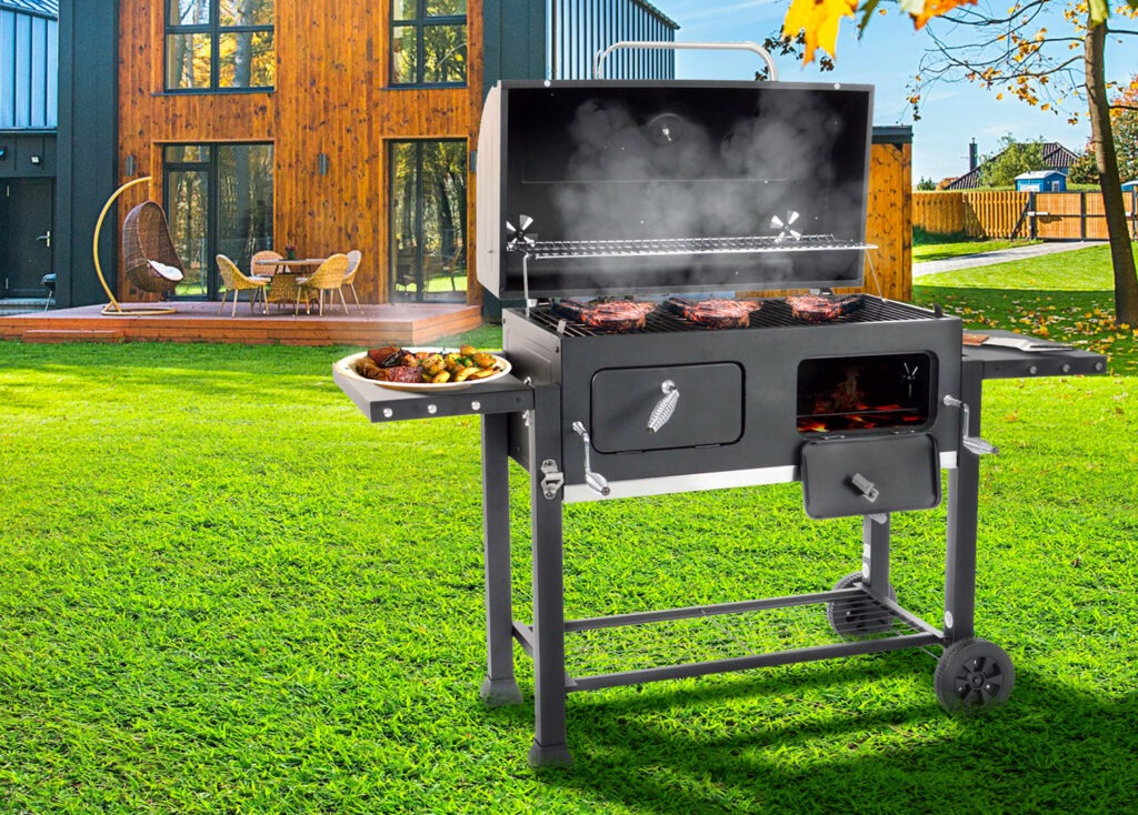 Ogród z nowoczesnym domem i grillem węglowym z otwartą pokrywą, na ruszcie cztery steki, na bocznej półce talerz z grillowanymi ziemniakami i mięsem, widoczny dym i ogień.