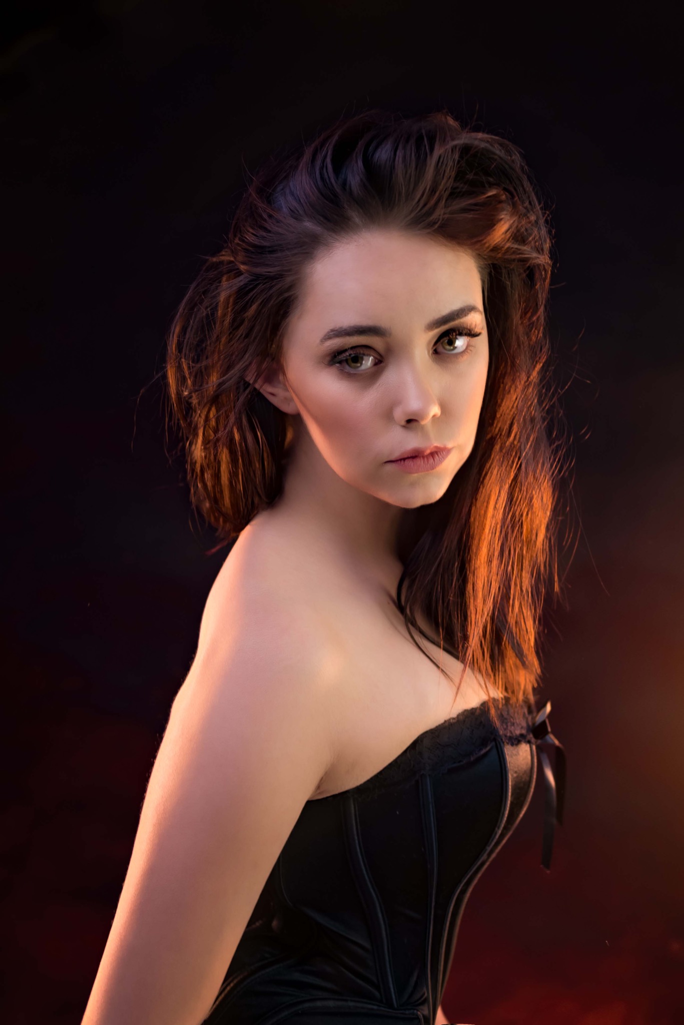 Portret kobiety w czarnym gorsecie na ciemnym tle z pomarańczowym podświetleniem włosów.