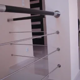 Nowoczesne schody z balustradą z poziomych, cienkich, metalowych prętów mocowanych do ściany, z czarnymi poręczami z metalowymi zakończeniami, widok z dołu na jasne wnętrze.