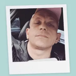 Portret mężczyzny w różowej czapce z daszkiem, siedzącego w samochodzie, zrobiony w stylu polaroid.