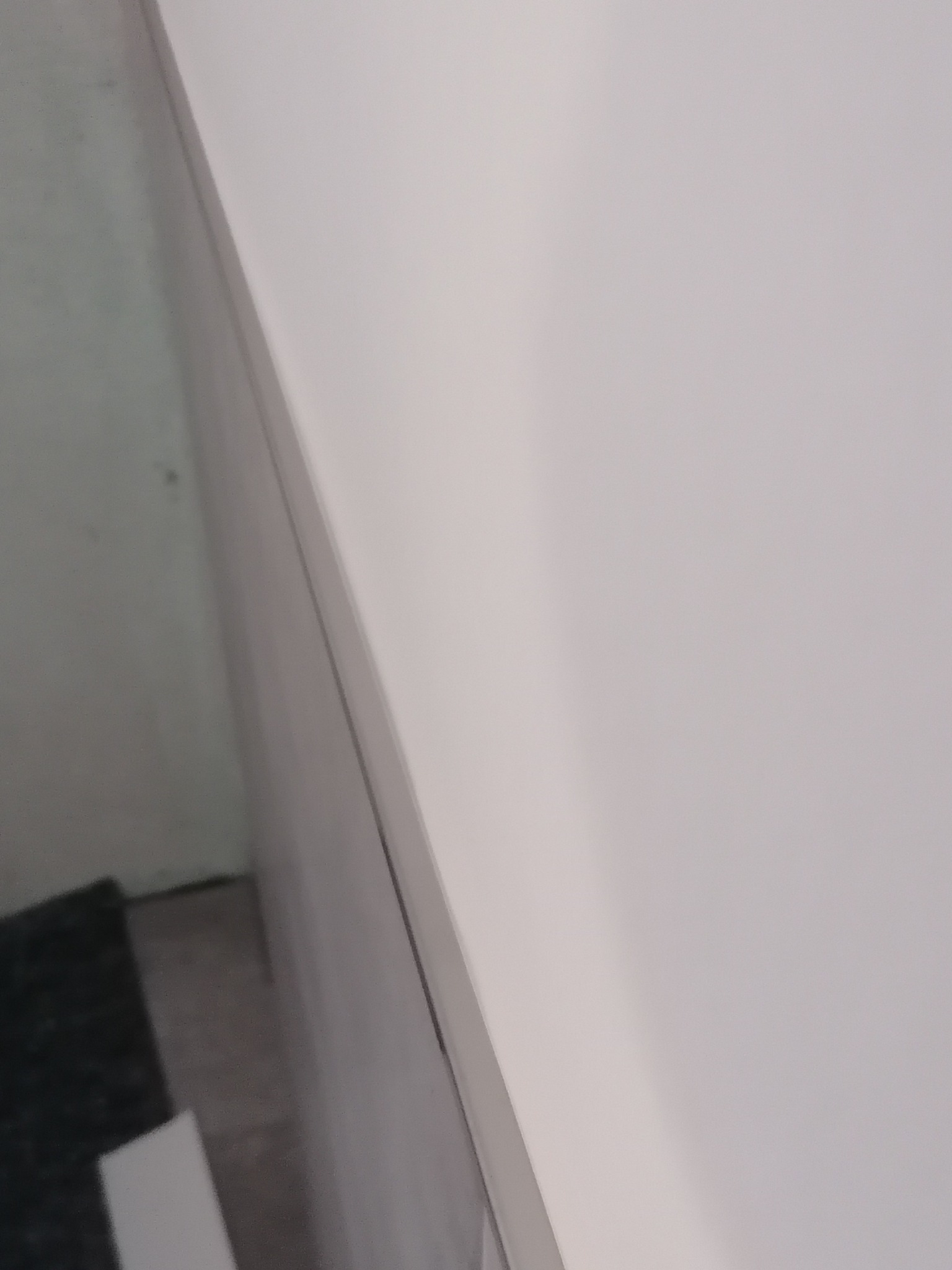 Fragment ściany po gładziowaniu, widoczny narożnik i fragment podłogi z ciemną wykładziną, ujęcie z dołu.