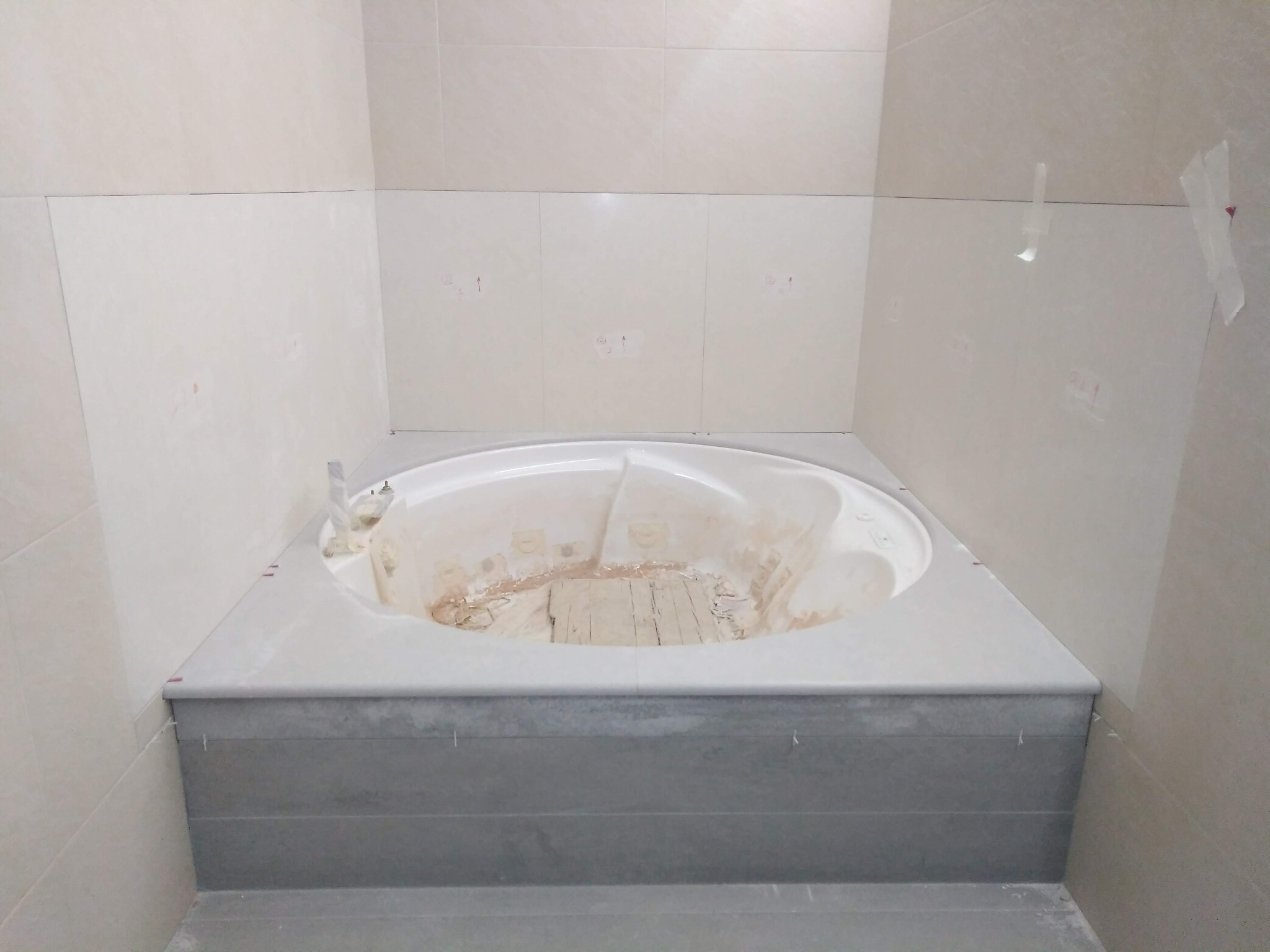 Wanna narożna w trakcie montażu, obłożona szarą mozaiką, widoczne płytki na ścianach z zaznaczonymi miejscami na otwory.