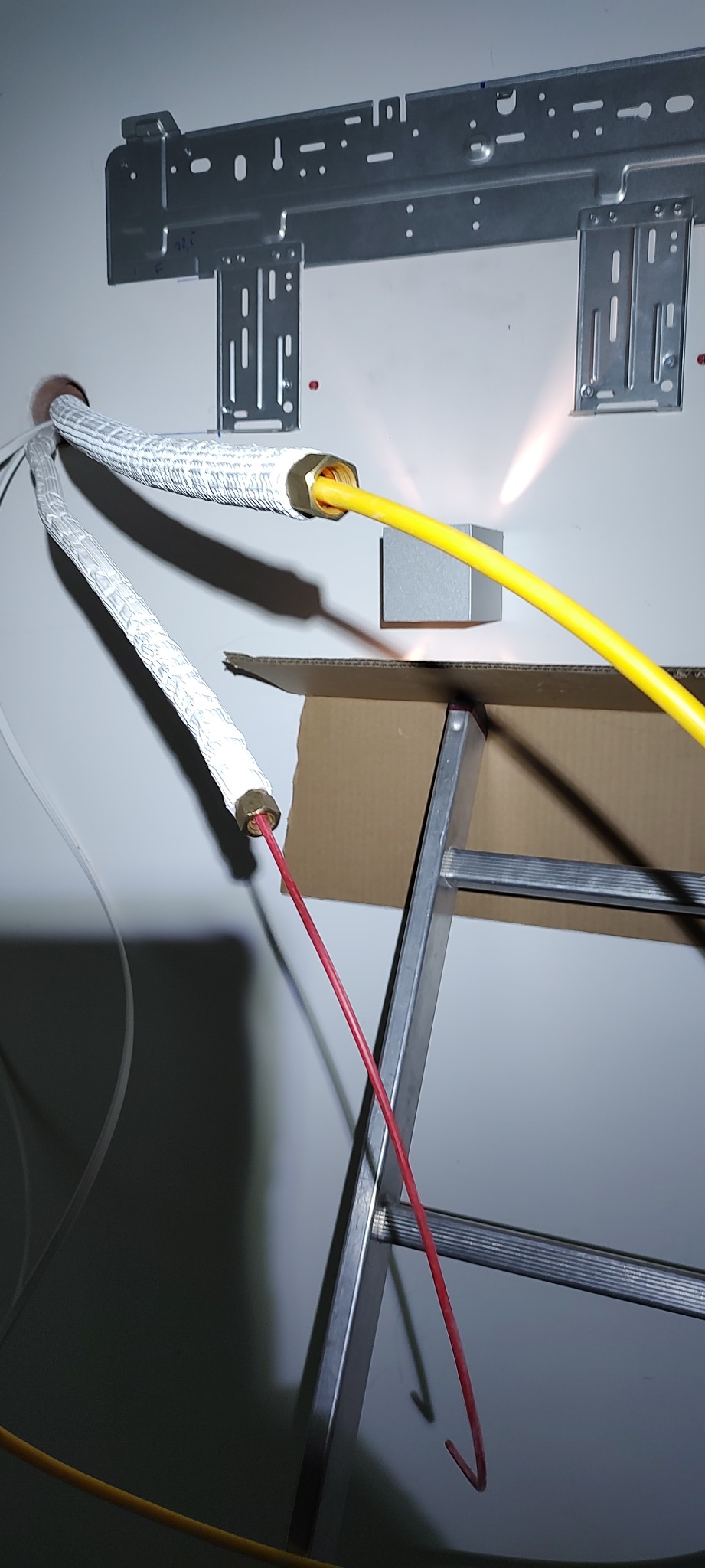 Montaż klimatyzacji: rury w izolacji termicznej i przewody elektryczne wychodzące ze ściany, widoczny metalowy stelaż montażowy i drabina aluminiowa.