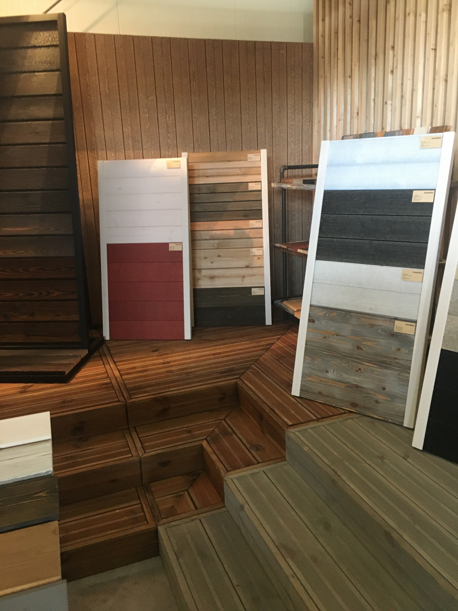 Ekspozycja próbek drewnianych elewacji i podłóg w różnych kolorach i fakturach, z widocznymi detalami konstrukcyjnymi podestu.