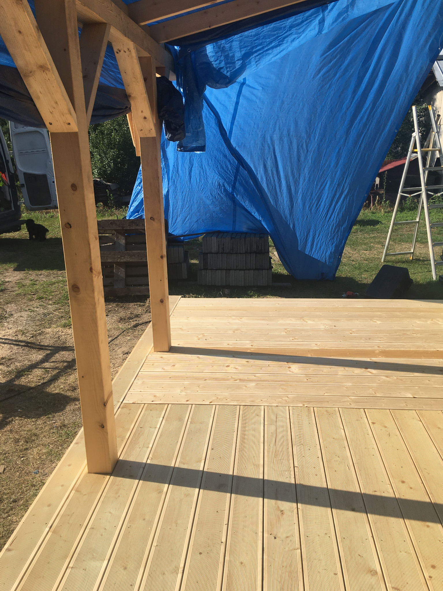 W Chmielowie powstaje drewniany taras z elementami konstrukcji szkieletowej, przykryty niebieską plandeką, widoczna drabina i samochód dostawczy.