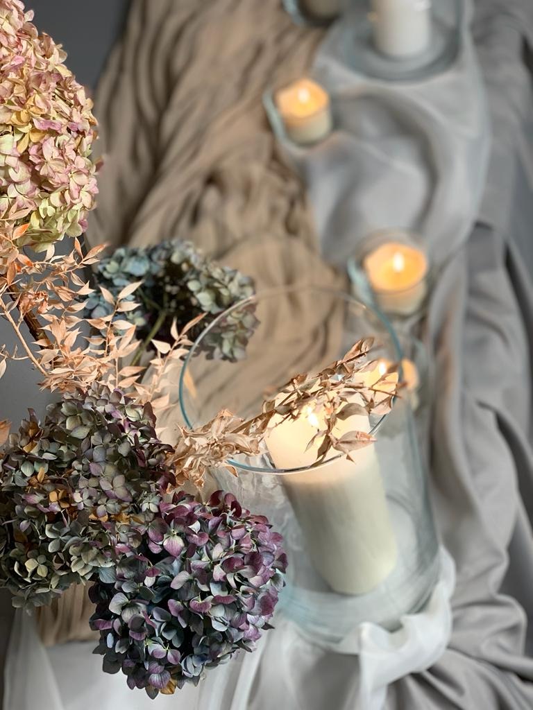 Dekoracja stołu w Woli z hortensjami i świecami w szklanych wazonach na tle drapowanej tkaniny.