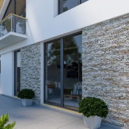 Elewacja budynku wykończona okładziną z kamienia naturalnego, widoczna z poziomu ogrodu z ozdobnymi krzewami i drzewami.