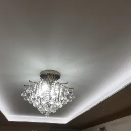 Kryształowy żyrandol zamontowany w podwieszonym suficie z ukrytym oświetleniem LED, widok z dołu.