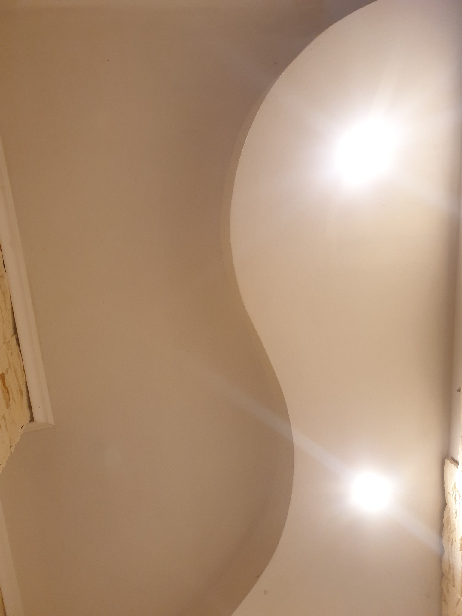 Fragment kremowego sufitu z dekoracyjną, falistą listwą oddzielającą dwie strefy oświetleniowe, z widocznymi dwoma punktowymi źródłami światła.