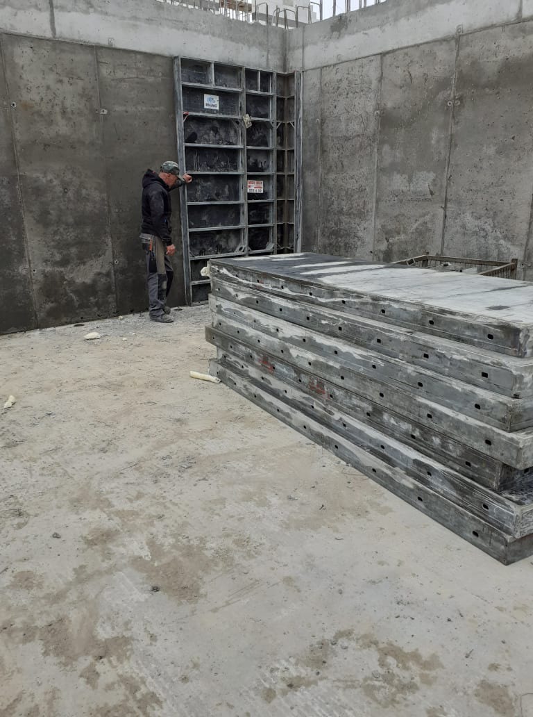 Konstrukcja szalunkowa zabetonowanej ściany fundamentowej w trakcie budowy domu, widoczny pracownik w czapce i roboczym ubraniu, obok stos płyt szalunkowych.