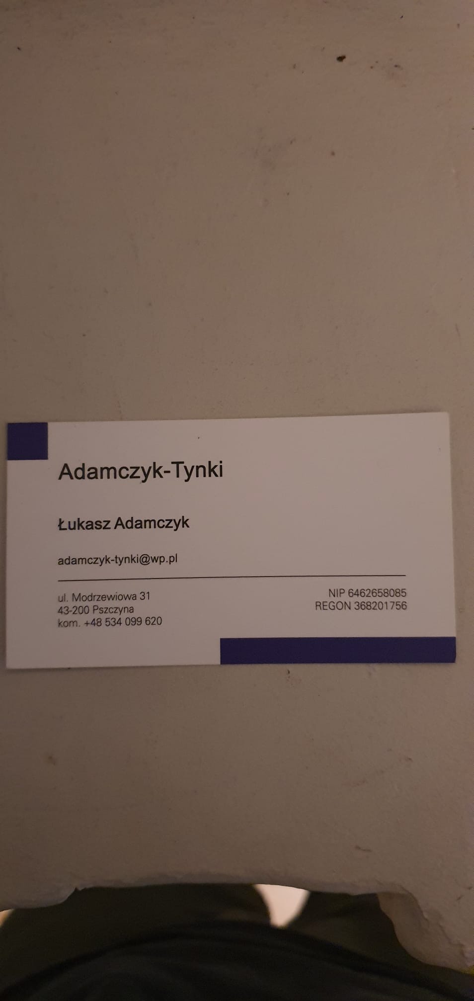 Wizytówka firmy Adamczyk-Tynki z danymi kontaktowymi, adresem, numerem telefonu, adresem e-mail, NIP i REGON, na jasnym tle.