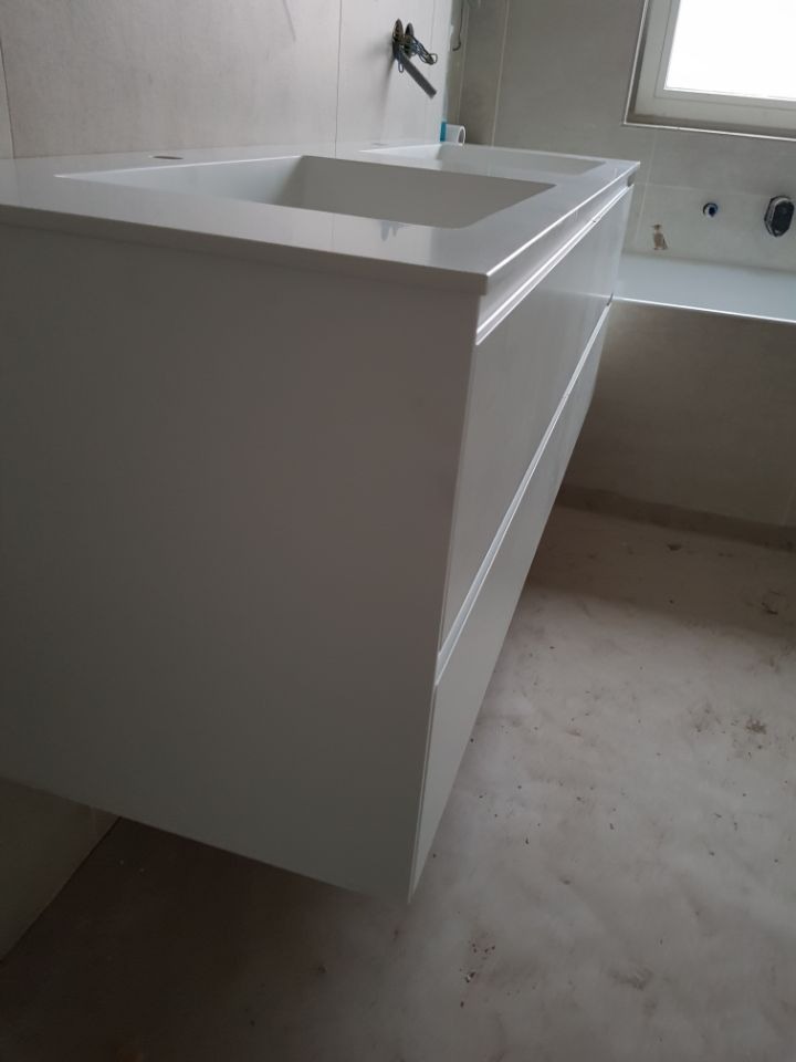 Biała, nowoczesna szafka umywalkowa z szufladami, zawieszona w łazience w trakcie remontu, widoczna wanna i okno w tle.