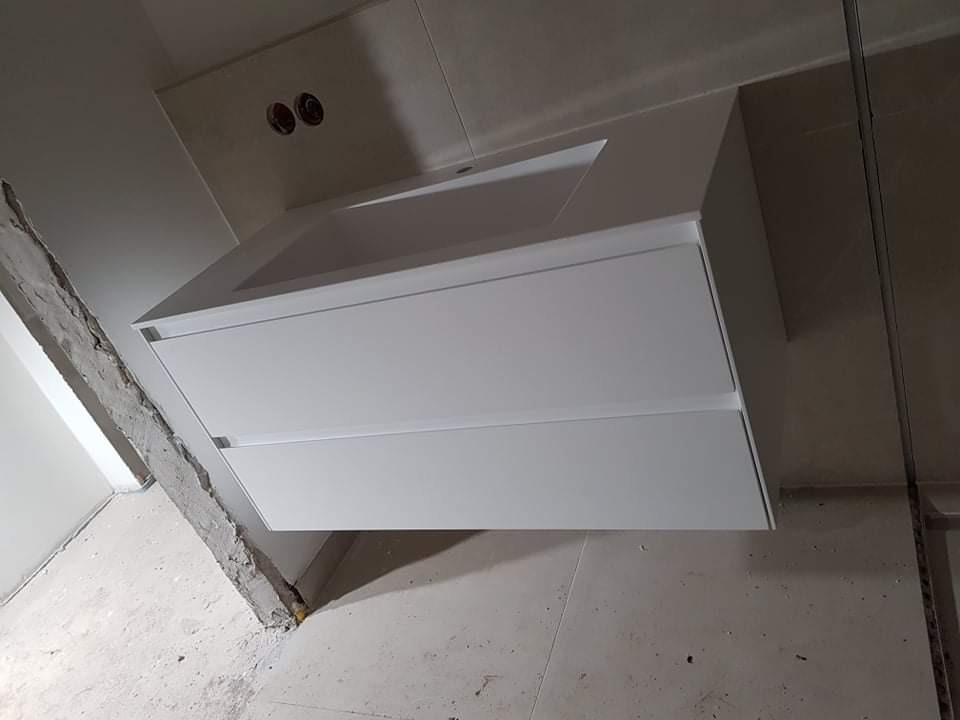 Biała, podwieszana szafka umywalkowa z dwiema szufladami, zamontowana w łazience w trakcie remontu, widoczne surowe ściany i podłoga.