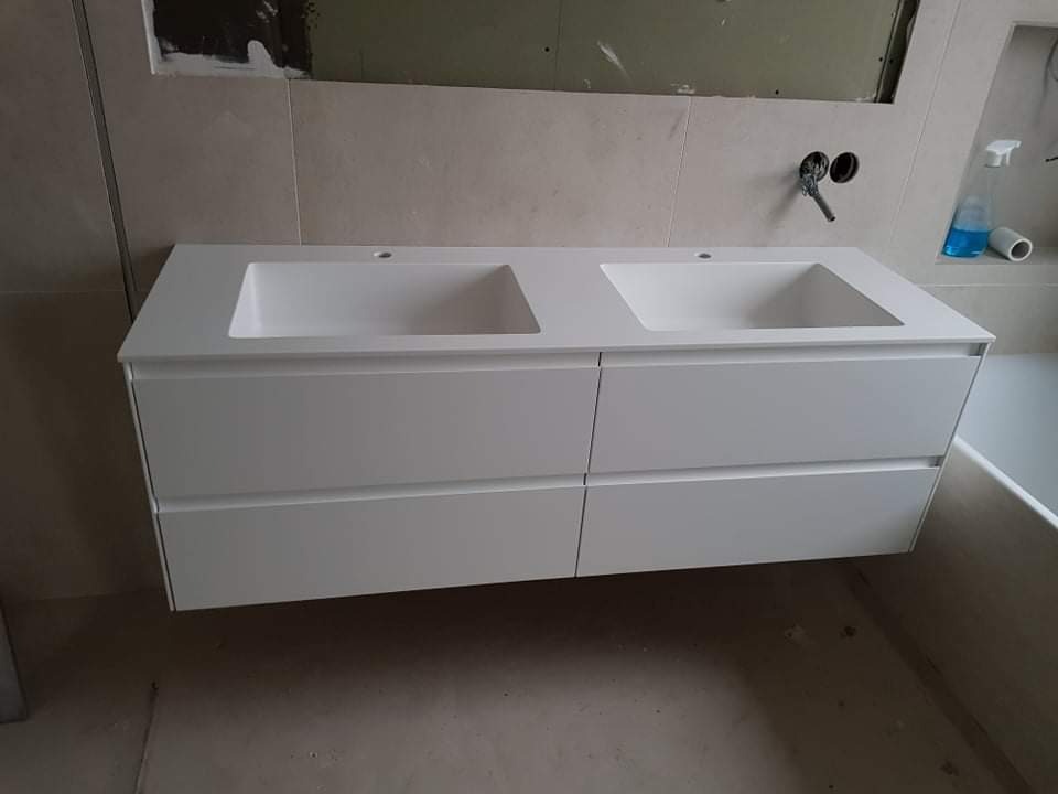 Biała szafka łazienkowa podwieszana z dwoma umywalkami, widoczne niedokończone prace wykończeniowe na ścianie i brak baterii.