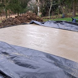 Bart-Bud - Wylana, świeża wylewka betonowa na zewnątrz, zabezpieczona czarną folią. W tle widoczna sterta ziemi i zieleń ogrodu. Widok z góry, lekko z ukosa.