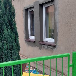 Bart-Bud - Dwa białe okna po wymianie, z widocznymi śladami świeżo nałożonej zaprawy na elewacji budynku. W tle zielony krzew i fragment zielonego ogrodzenia.