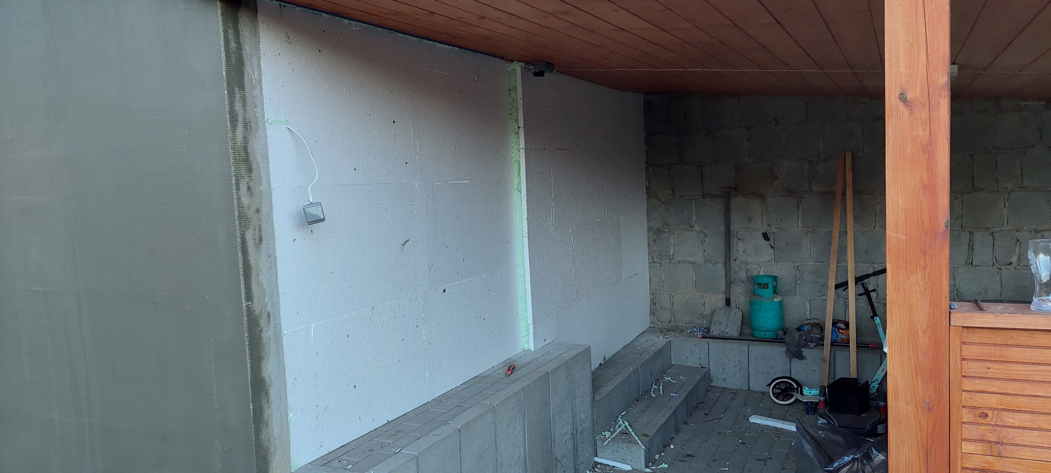 Ocieplanie ściany styropianem w Gostyniu, widoczna siatka i klej. Fragment ściany otynkowany, sufit drewniany. Prace wykończeniowe w trakcie realizacji.