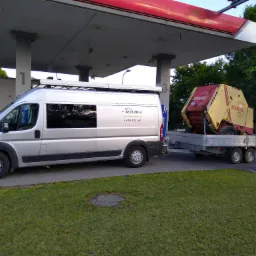 Srebrny bus firmy Polbud z przyczepą z maszyną rolniczą marki Krone pod wiatą stacji benzynowej Verva.