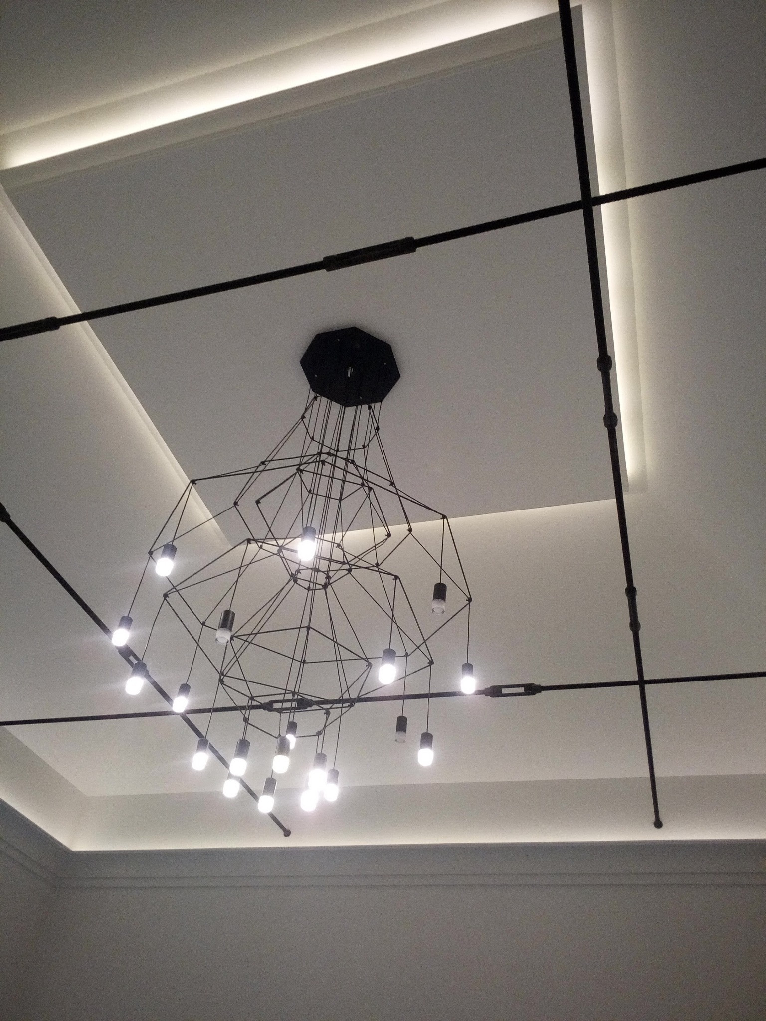 Nowoczesny żyrandol z wieloma żarówkami zawieszony na suficie z podświetleniem LED, czarne metalowe elementy konstrukcyjne.