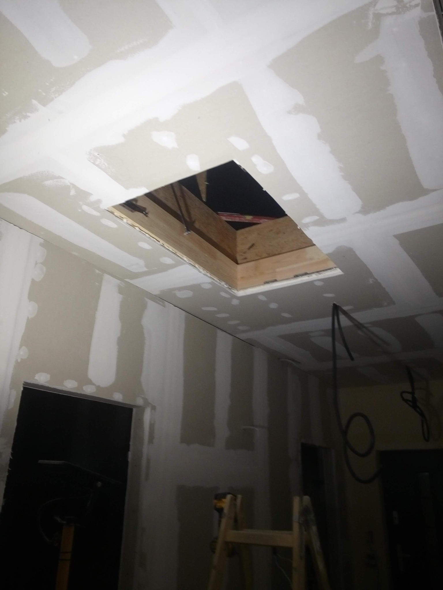 Poddasze w trakcie ocieplania z widocznym otworem w suficie i częściowo wykończonymi ścianami karton-gips z nałożonymi paskami gipsu.