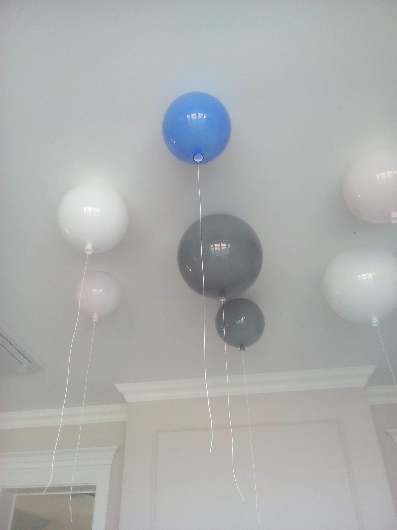 Kolorowe balony helowe, białe, szare, różowe i niebieskie, przymocowane do sufitu w jasnym pomieszczeniu z ozdobnymi sztukateriami.