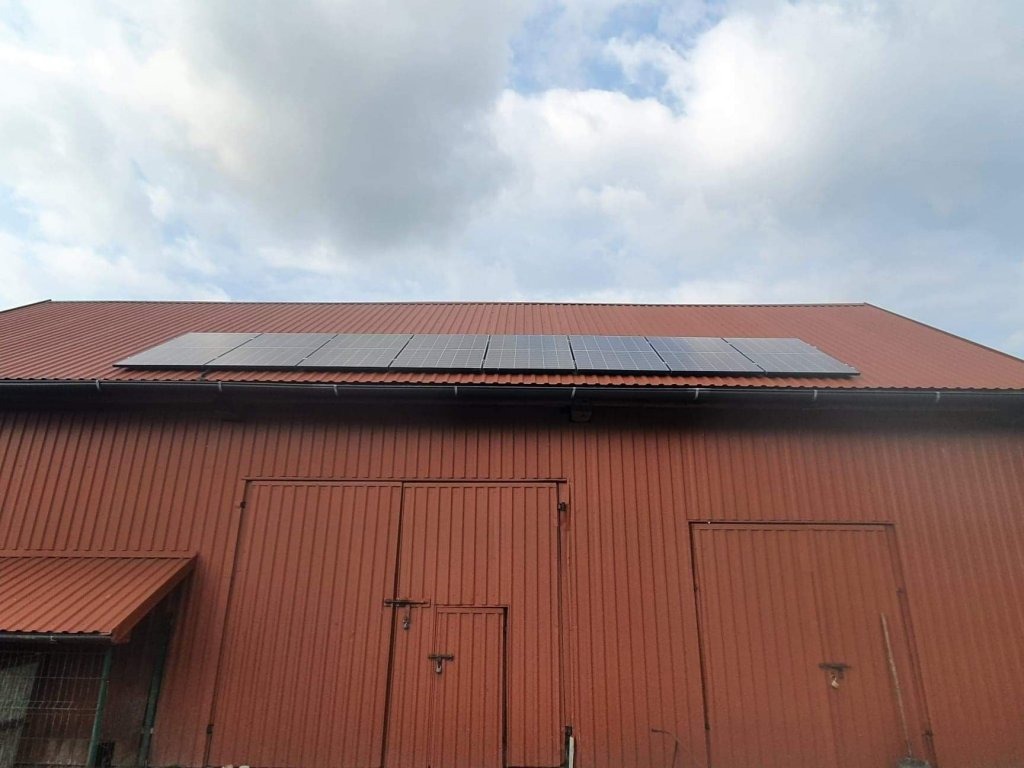 Panele słoneczne na dachu budynku gospodarczego w Wolbromiu, widoczne metalowe drzwi i pochmurne niebo.