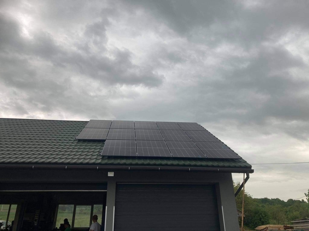 Panele słoneczne zamontowane na dachu garażu z blachodachówki w pochmurny dzień.