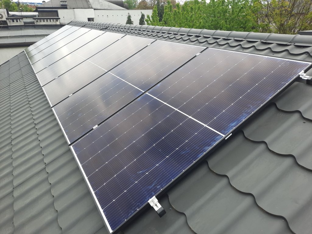 Panele fotowoltaiczne zamontowane na dachu z blachodachówki w kolorze grafitowym, widok z góry pod kątem, z widocznymi elementami montażowymi.