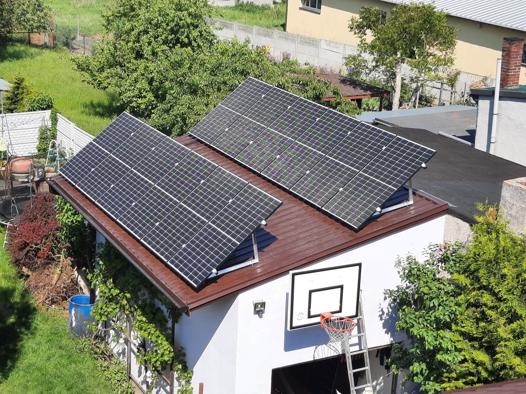 Dwa panele słoneczne na dachu budynku gospodarczego z brązowym dachem, na ścianie budynku kosz do koszykówki, widok z góry.