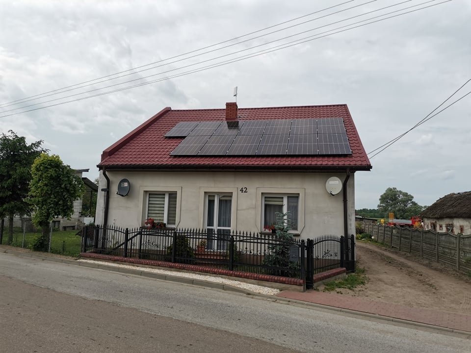 Dom jednorodzinny z panelami słonecznymi na czerwonym dachu, widoczne satelity na ścianie i numer domu 42.