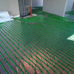 NIKIEL INSTALACJE SANITARNE, C.O., GAZ - Zielone rury ogrzewania podłogowego ułożone w pętle na folii z siatką, widoczne ściany w stanie surowym i izolacja ze styropianu.