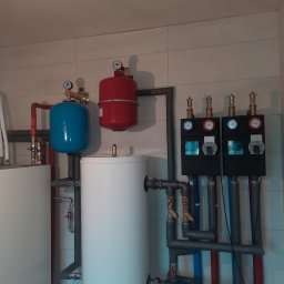 NIKIEL INSTALACJE SANITARNE, C.O., GAZ - Instalacja grzewcza z dwoma zbiornikami buforowymi (biały i niebieski), czerwonym naczyniem przeponowym, rozdzielaczem z czterema obiegami grzewczymi, rurami w kolorach czerwonym i niebieskim...