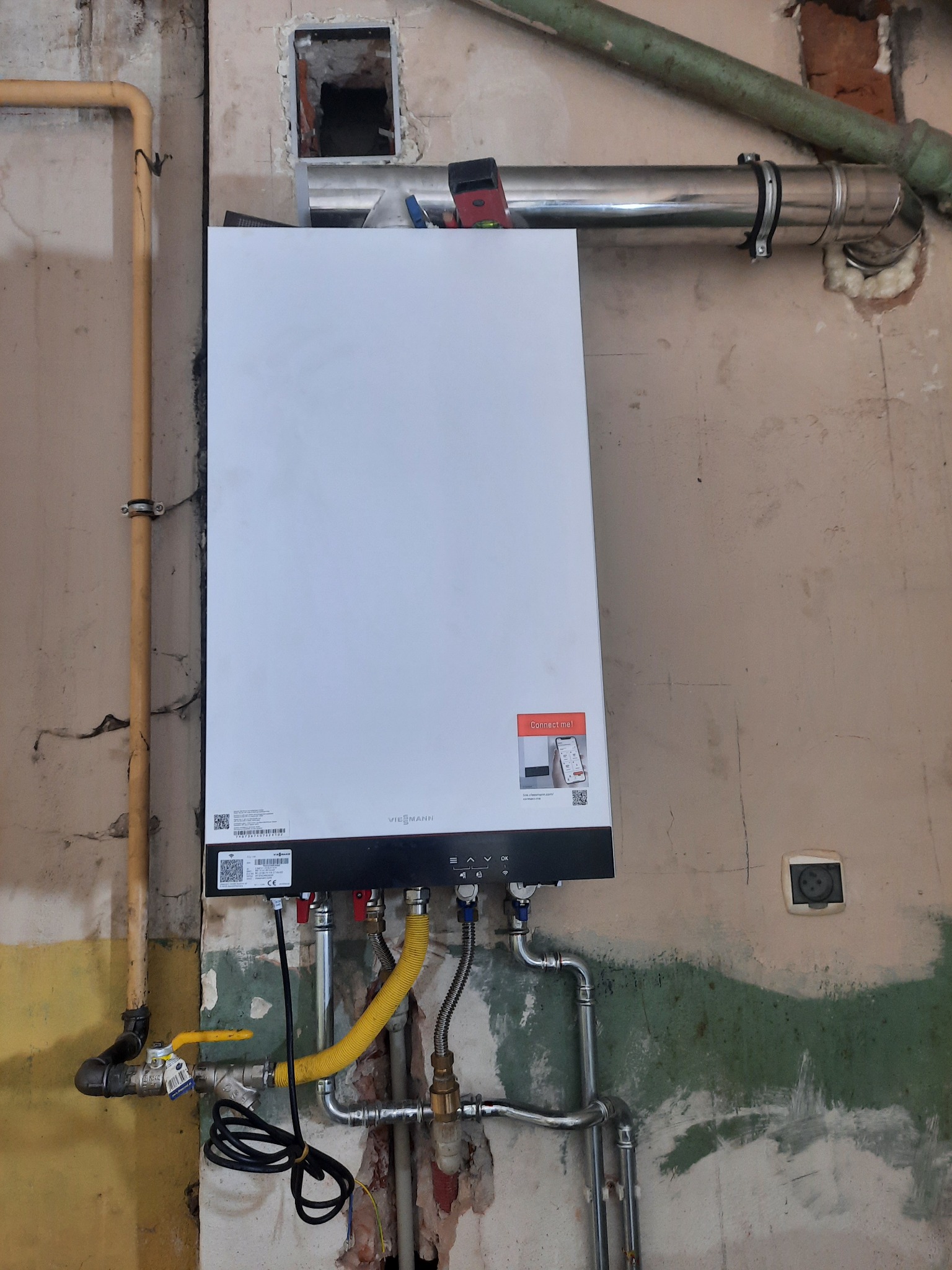 Nowy, biały piec gazowy Viessmann zamontowany na surowej ścianie podczas instalacji, widoczne żółte i stalowe rury gazowe oraz instalacja odprowadzania spalin.