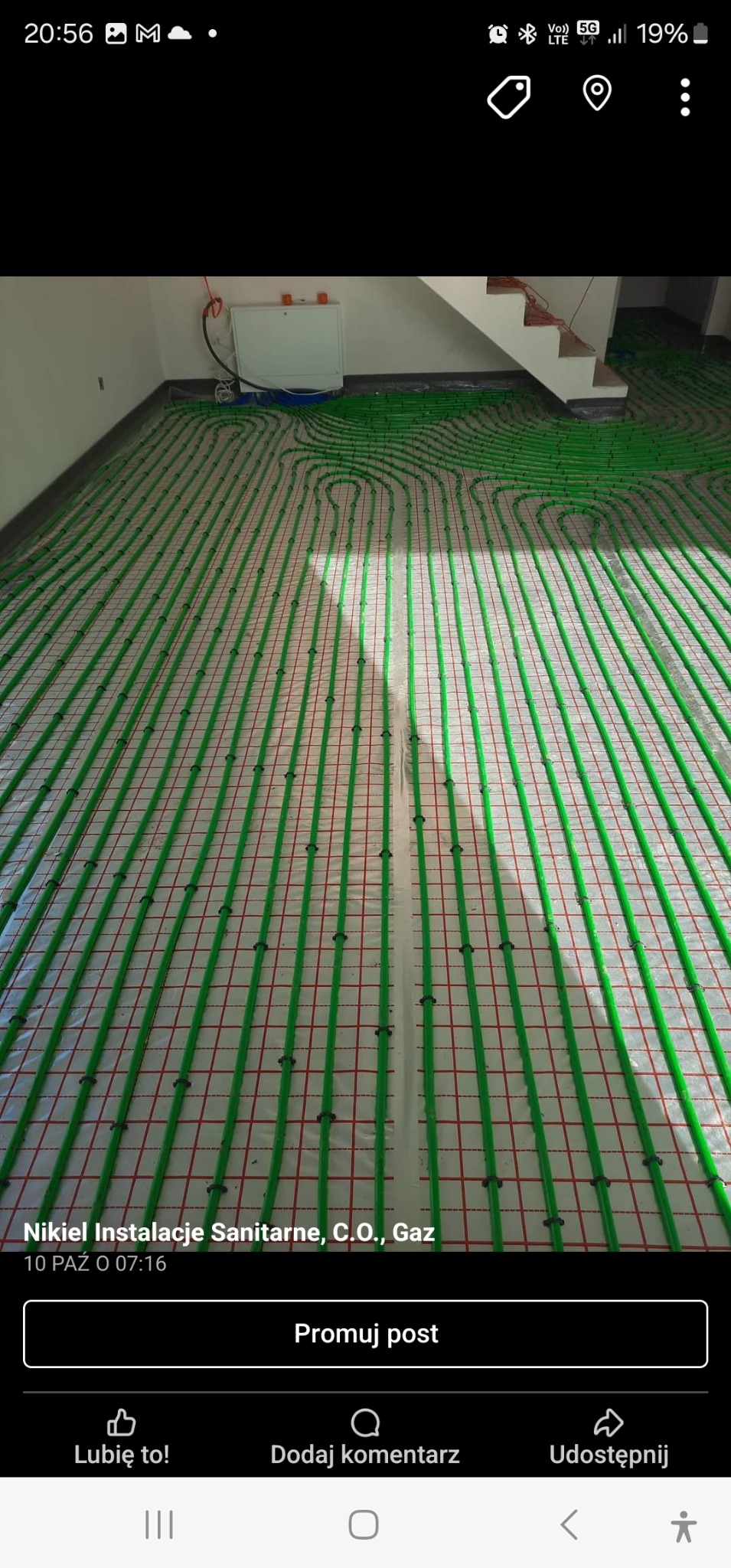 Zielone rury ogrzewania podłogowego ułożone na folii z czerwoną siatką, widok z góry, w tle biała ściana i schody.