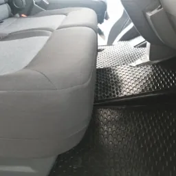 Szare siedzenie i czarne gumowe dywaniki z wzorem plastra miodu w samochodzie dostawczym, widoczne z niskiego kąta.