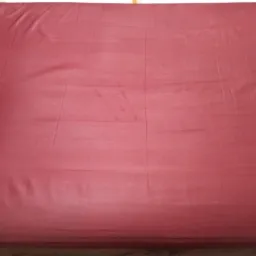 Czerwona tapicerka materaca z widocznymi śladami użytkowania i lekkimi zmarszczeniami.