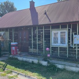 REHinstal Sebastian Szpunar - Ocieplanie drewnianego domu w Rzeszowie. Widoczne rusztowanie, puszki z wełną mineralną Rockwool i pracownik w trakcie montażu izolacji. Prace remontowe.