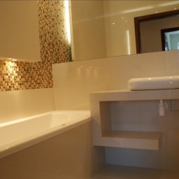 Mkbud - Nowoczesna łazienka z wanną, umywalką nablatową na szafce z półkami i mozaiką na ścianie, odbicie lustra w tle.