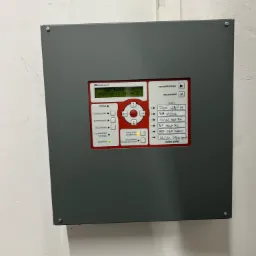 Szary panel sterowania systemem alarmowym Polon-Alfa IGNIS 2040 na ścianie, z ekranem wyświetlającym datę i godzinę, przyciskami funkcyjnymi oraz listą stref z odręcznymi notatkami.