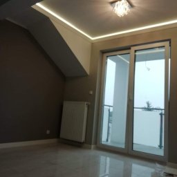 KAMIREM - Jasne, błyszczące płytki podłogowe w pokoju na poddaszu z oknem balkonowym, grzejnikiem i nowoczesnym oświetleniem LED w suficie pod skosem.