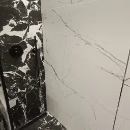 Nowoczesna kabina prysznicowa z czarno-białymi płytkami imitującymi marmur, czarna armatura, widok z dołu