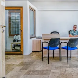 Wnętrze biura z ekspozycją drzwi wewnętrznych z przeszkleniami, widoczne okno PCV i pracownik za biurkiem.