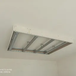 Sufit podwieszany z płyt kartonowo-gipsowych na metalowej konstrukcji, widoczne profile i płyty, w tle biały sufit i ściany przed wykończeniem.