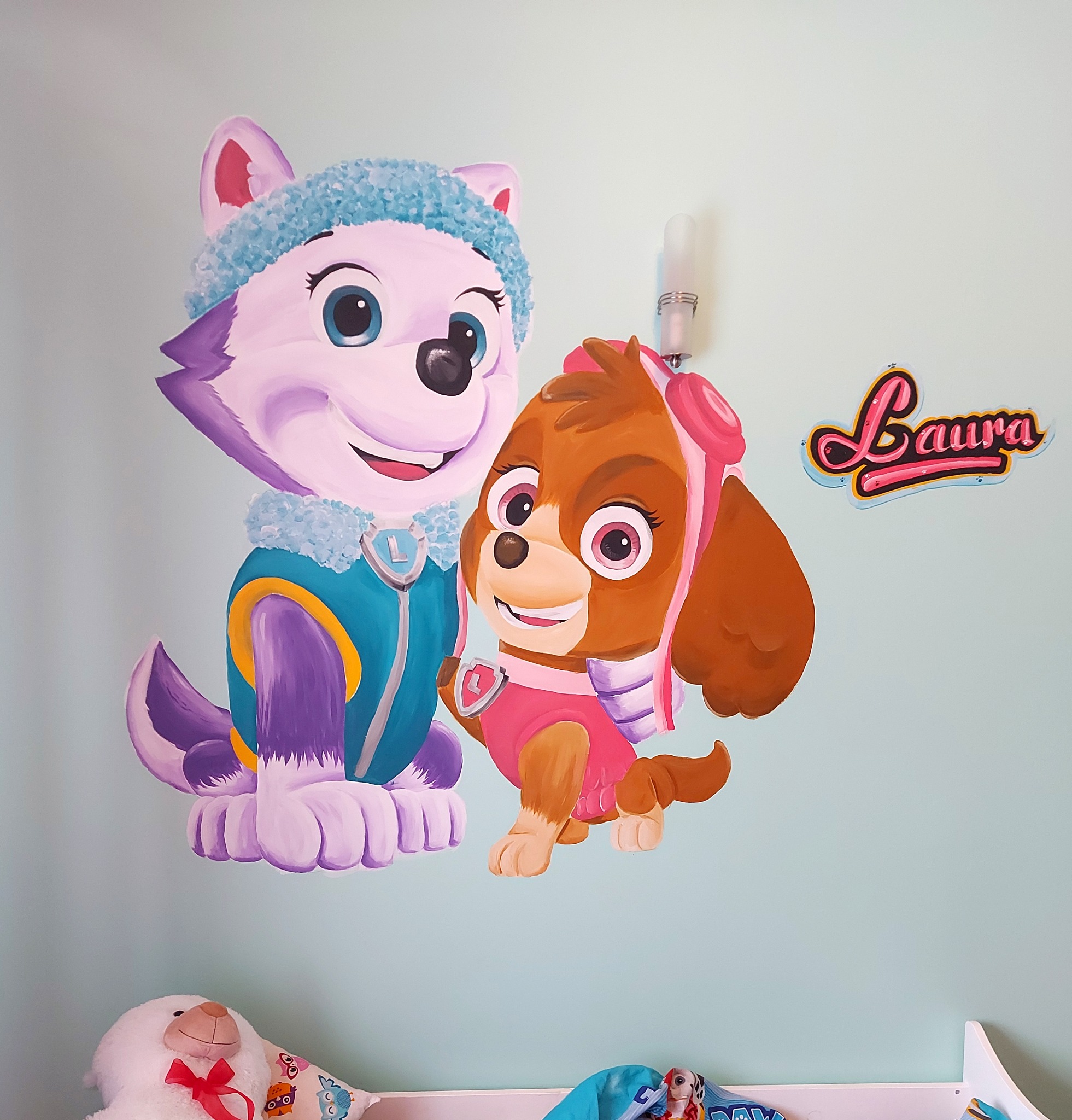 Ręcznie malowana ściana w pokoju dziecięcym z postaciami z bajki Psi Patrol: Everest i Skye oraz imieniem Laura.