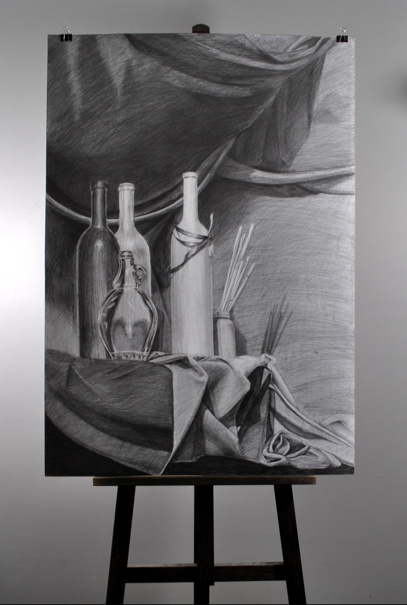 Ręcznie rysowany ołówkiem martwa natura z butelkami, dzbankiem i draperia na sztaludze z widocznymi klamrami mocującymi.