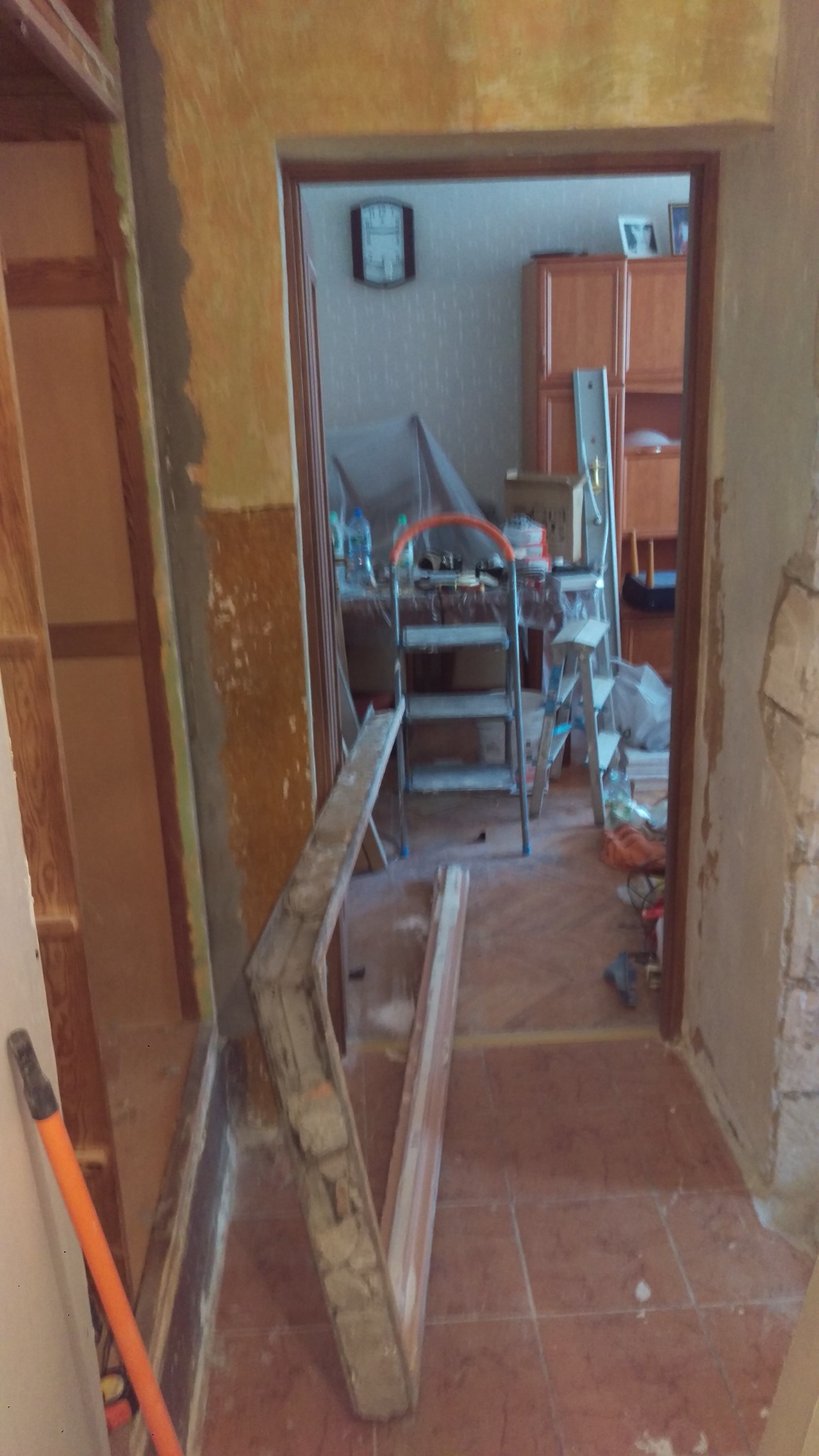 Demontaż ościeżnicy w trakcie prac remontowych, widoczne fragmenty starej ściany i podłogi z płytek, drabina w tle.
