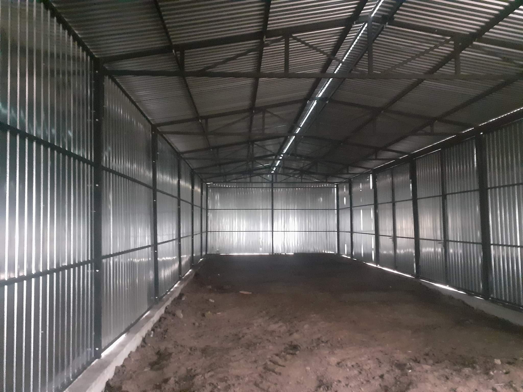 Wnętrze nowo wybudowanej hali z metalową konstrukcją i ścianami z blachy falistej, widoczne surowe podłoże gruntowe.